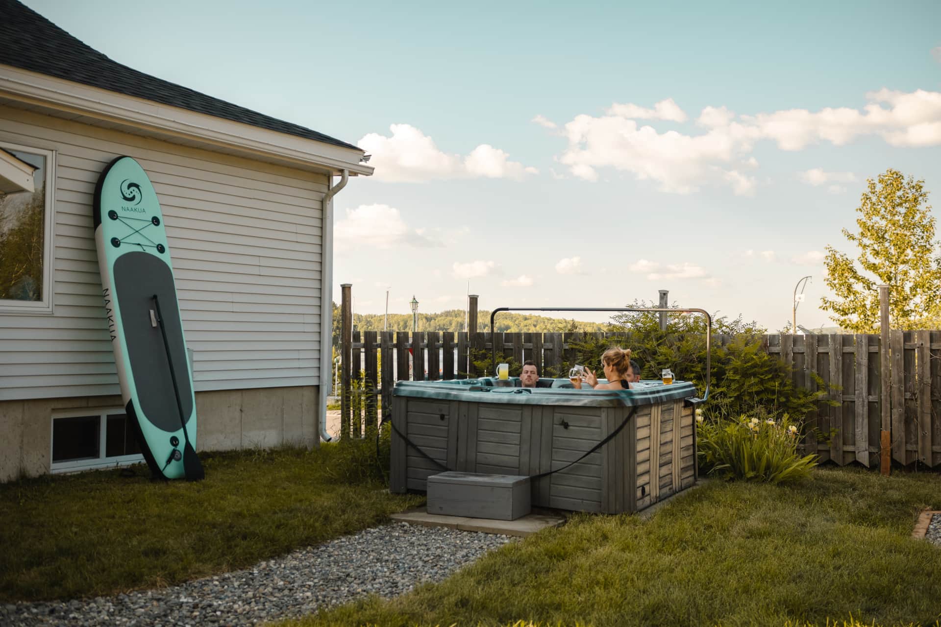 Couple dans le spa d'un chalet bord du lac Mégantic en été, planche SUP et vue sur les collines