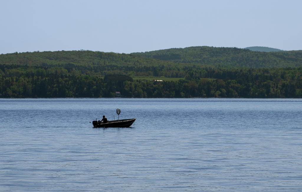 Pêcheur en chaloupe sur le lac Mégantic en été, collines boisées des Appalaches en arrière-plan